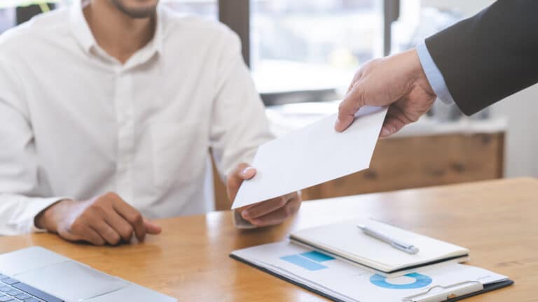 A person handing an envelope to another person in a business setting.