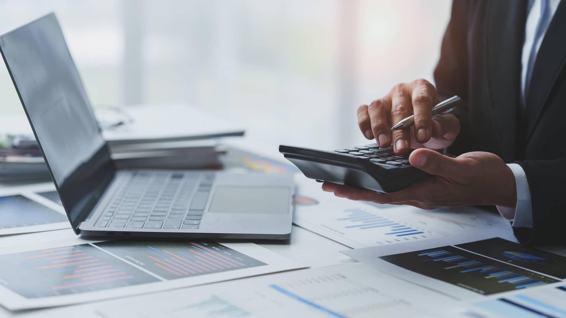 Geschäftsperson mit Taschenrechner, Laptop und Finanzdokumenten analysiert Rechnungsanforderungen.