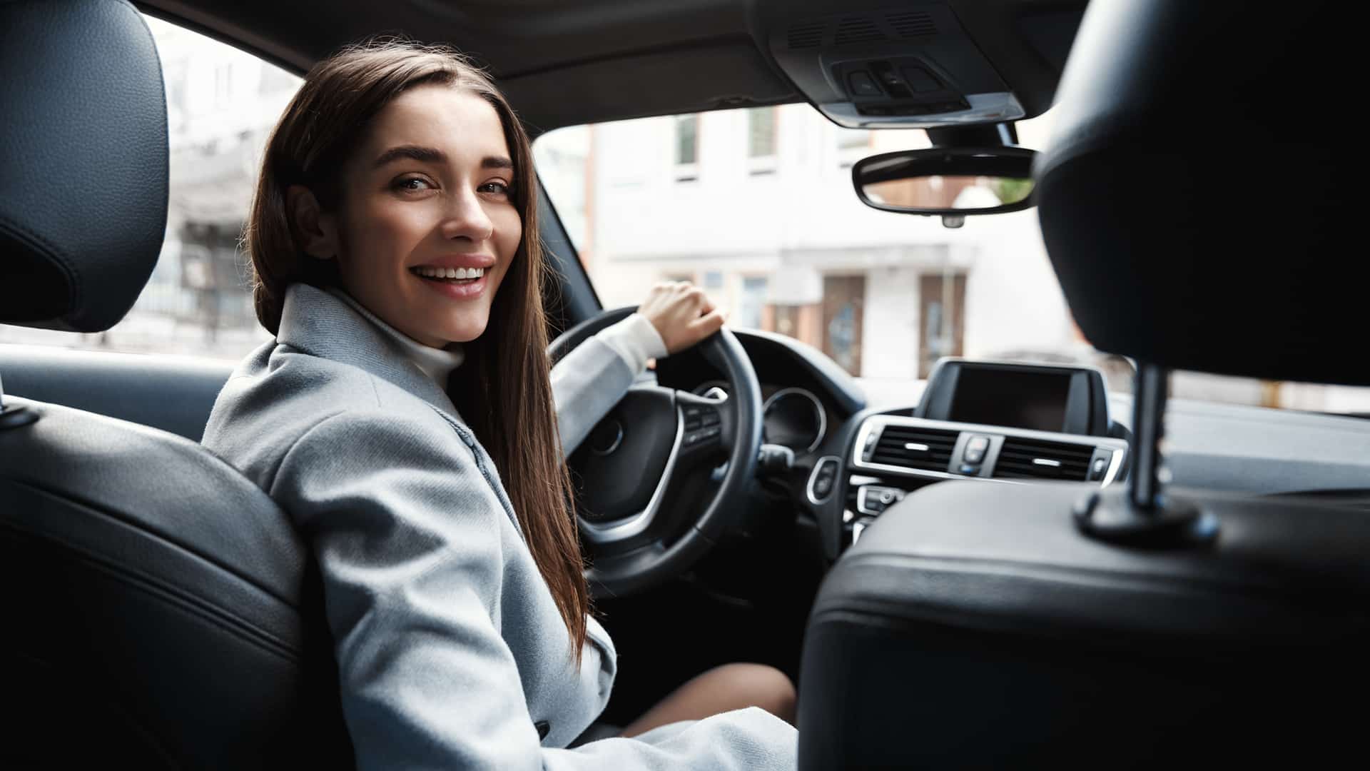 Našmiješena poslovna žena za volanom modernog automobila, gleda prema kameri.