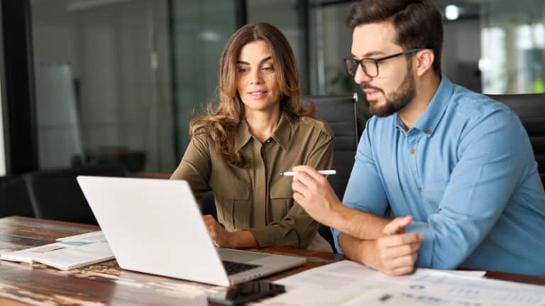 Two business professionals reviewing tax documents together on a laptop in a modern office.