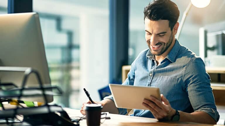Geschäftsmann mit Tablet am Schreibtisch überprüft Steuerneuigkeiten für Oktober.