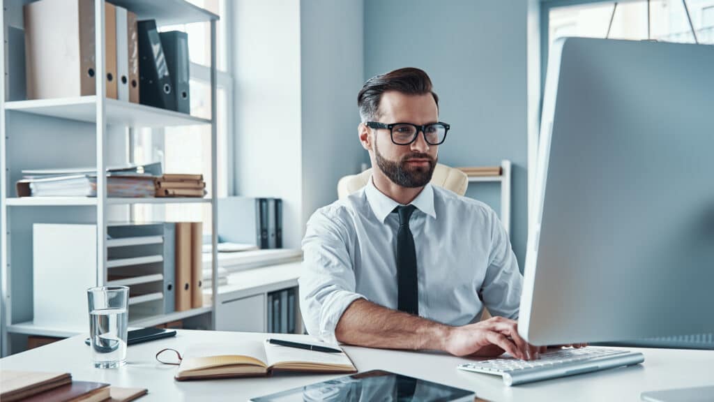 Business professional working at a computer in an office while reviewing tax information and documentation.
