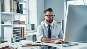 Business professional working at a computer in an office while reviewing tax information and documentation.