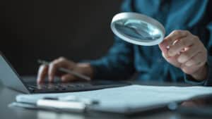 Business professional reviewing financial documents with a magnifying glass, analyzing company results and decisions on profit distribution or loss coverage.