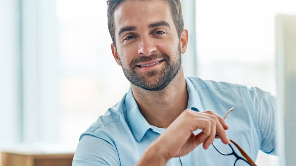 Lächelnder Business-Profi in einem modernen Büro hält eine Brille in der Hand und steht für die offene Position als Payroll Specialist bei CONEO Croatia.