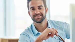 Lächelnder Business-Profi in einem modernen Büro hält eine Brille in der Hand und steht für die offene Position als Payroll Specialist bei CONEO Croatia.